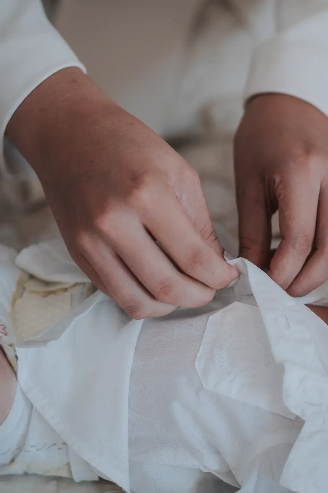 Vestizione prima del battesimo: le mani che chiudono il vestitino del bambino