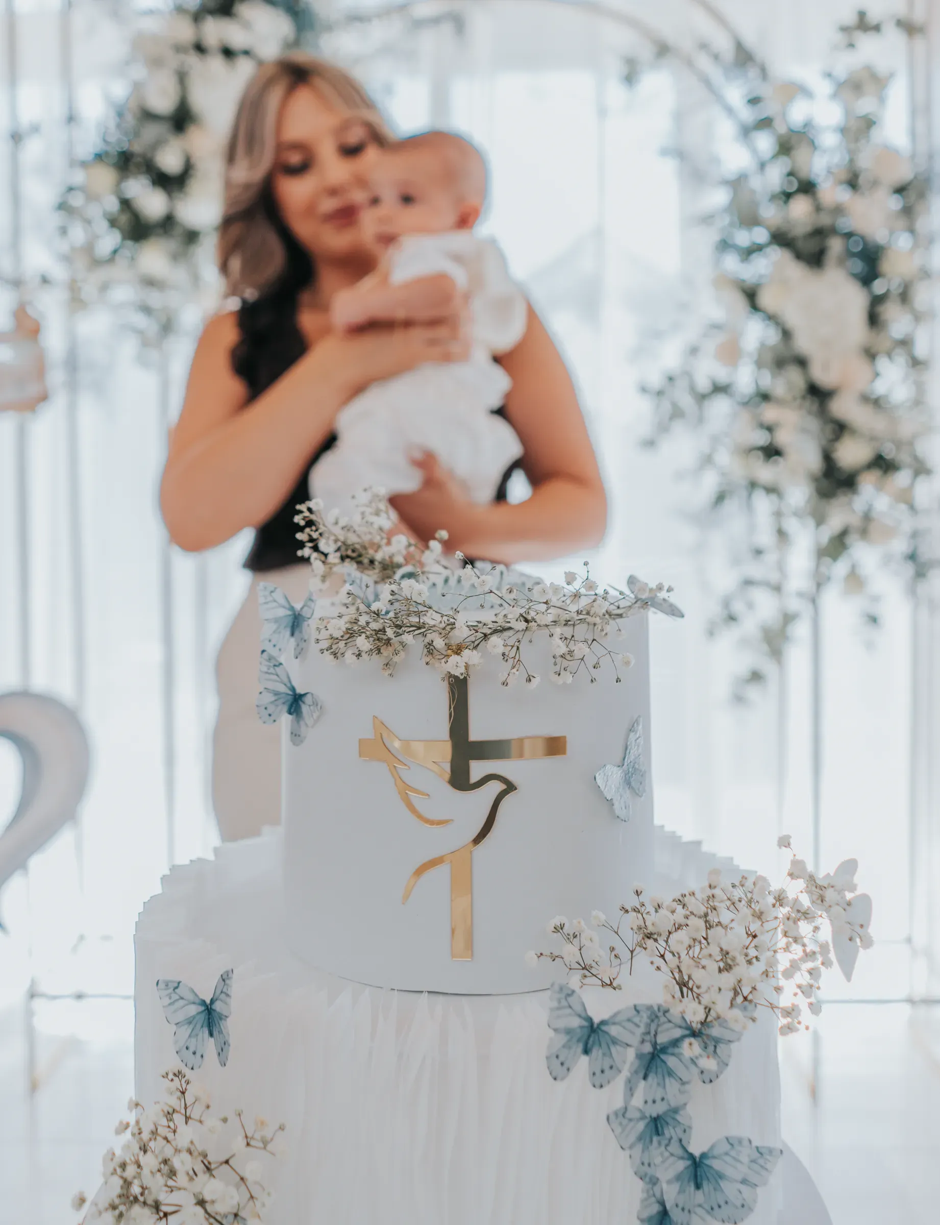 Torta di battesimo con croce e colomba: sullo sfondo la mamma con il bambino in braccio
